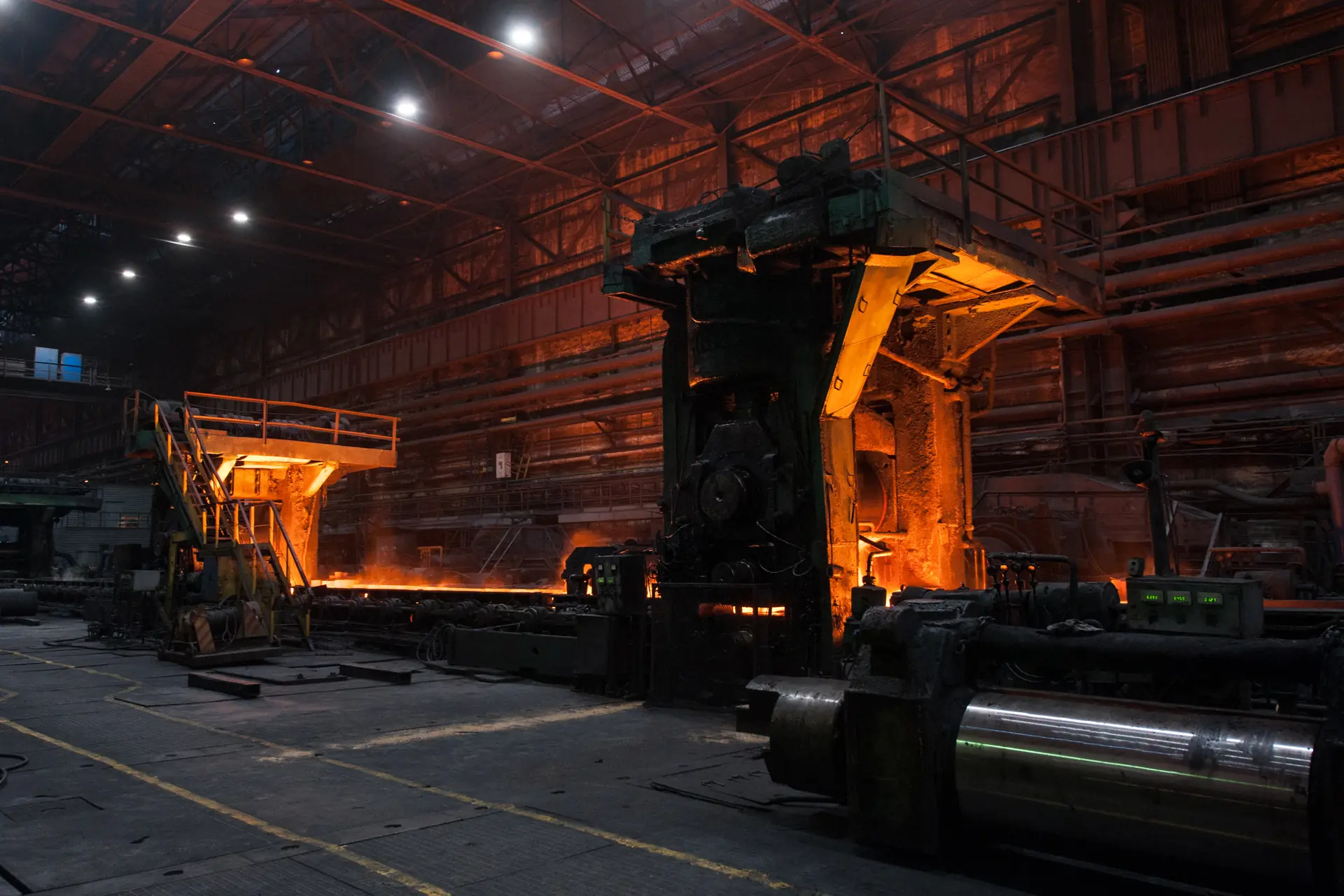 Dunkle Werkshalle mit Walzgerüst, im Hintergrund glühendes Metall